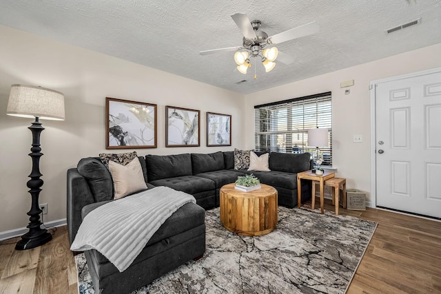 living area with a ceiling fan, baseboards, wood finished floors, visible vents, and a textured ceiling