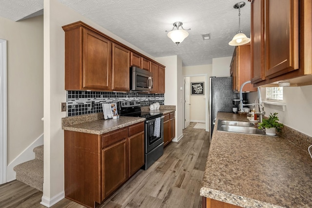 kitchen with appliances with stainless steel finishes, decorative light fixtures, sink, decorative backsplash, and light hardwood / wood-style flooring