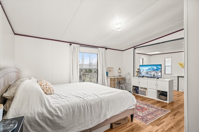 bedroom featuring vaulted ceiling, a textured ceiling, and light wood-type flooring