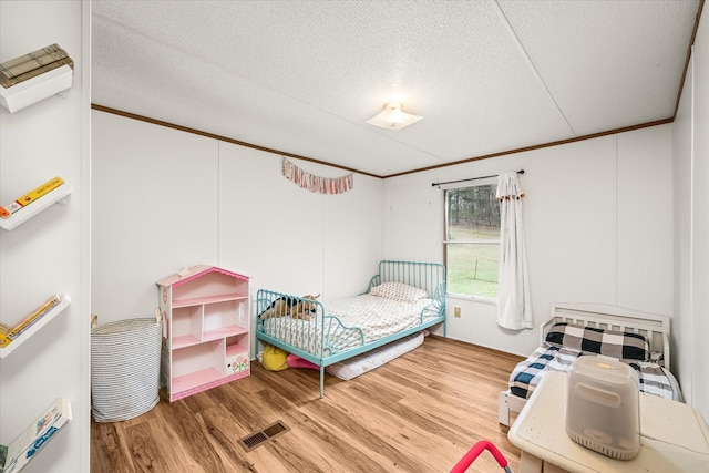 bedroom featuring hardwood / wood-style floors, crown molding, and a textured ceiling