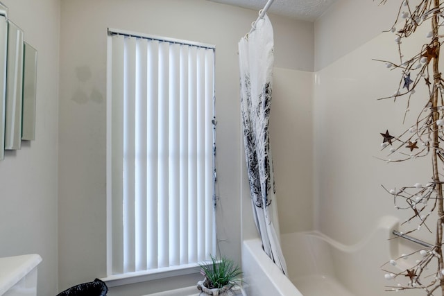 bathroom with toilet, shower / bathtub combination with curtain, and a textured ceiling