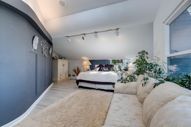 bedroom featuring rail lighting, lofted ceiling, and light wood-type flooring