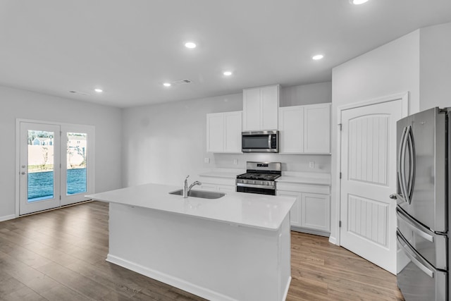 kitchen featuring sink, appliances with stainless steel finishes, a kitchen island with sink, light hardwood / wood-style floors, and white cabinets