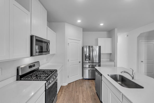 kitchen featuring sink, white cabinetry, light stone counters, wood-type flooring, and appliances with stainless steel finishes