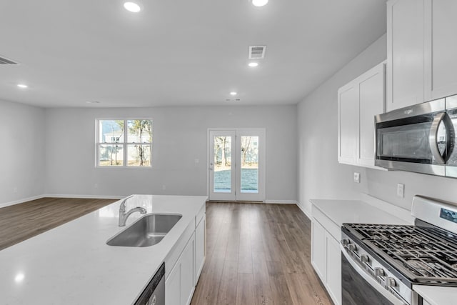 kitchen with stainless steel appliances, sink, wood-type flooring, and white cabinets