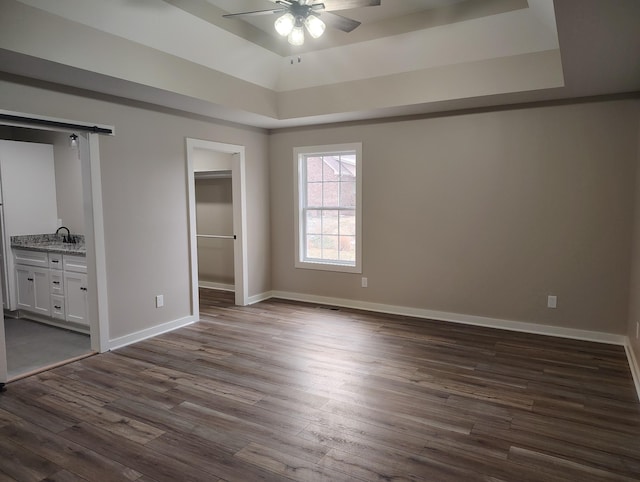 unfurnished bedroom with a barn door, a spacious closet, ceiling fan, and a tray ceiling