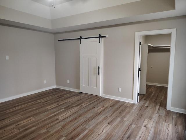 unfurnished bedroom featuring wood-type flooring, a barn door, a closet, and a tray ceiling