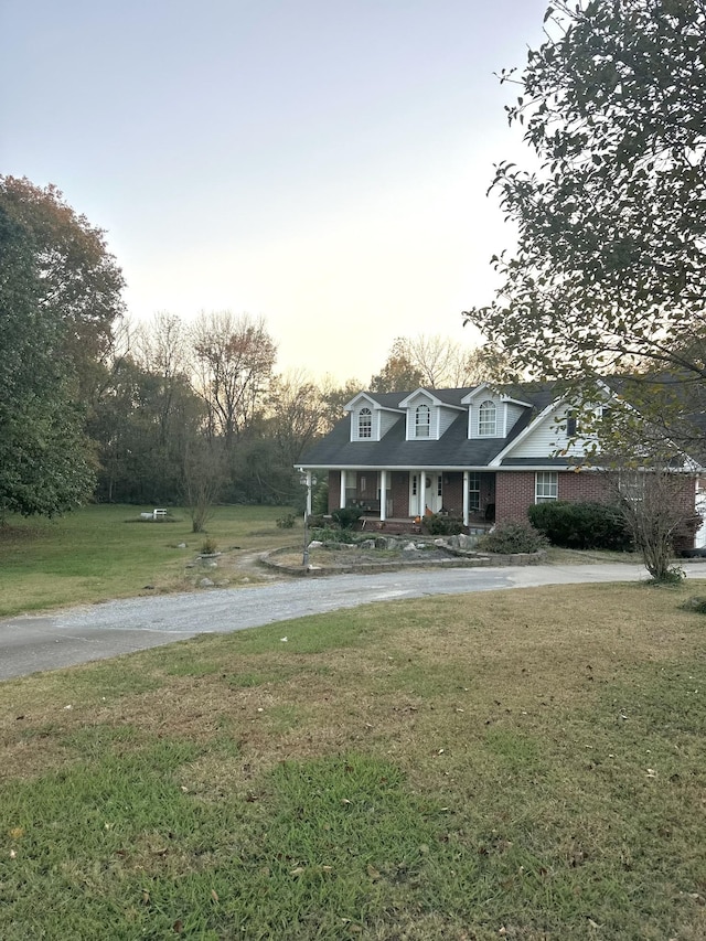 cape cod-style house with covered porch and a lawn