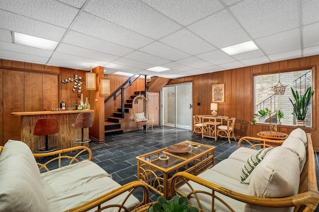 living room featuring a paneled ceiling, wooden walls, and bar area