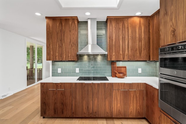 kitchen featuring light hardwood / wood-style flooring, backsplash, double oven, and wall chimney exhaust hood