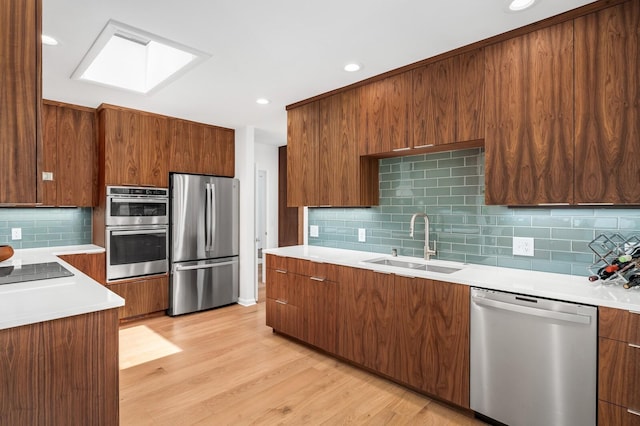 kitchen with sink, appliances with stainless steel finishes, a skylight, tasteful backsplash, and light hardwood / wood-style floors