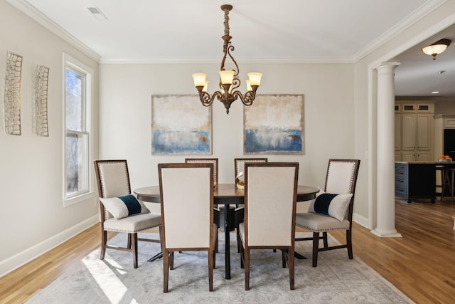 dining room with a notable chandelier, ornamental molding, ornate columns, and light wood-type flooring