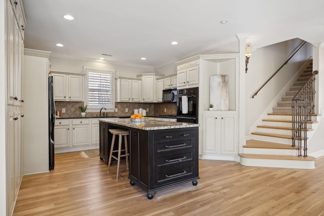 kitchen featuring light hardwood / wood-style floors, a center island, a kitchen bar, and black appliances