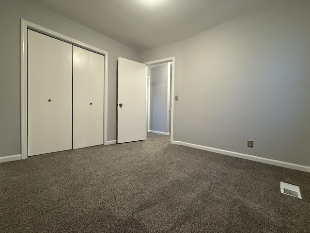 unfurnished bedroom with dark carpet and a closet