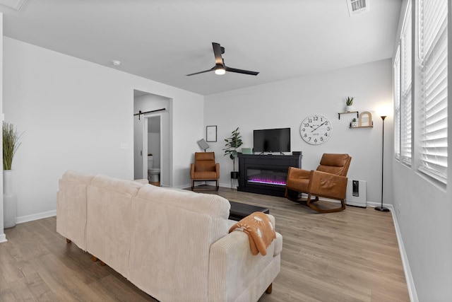 living room with light hardwood / wood-style floors, a barn door, and ceiling fan