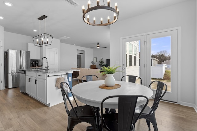 dining area featuring sink, ceiling fan with notable chandelier, and light hardwood / wood-style floors