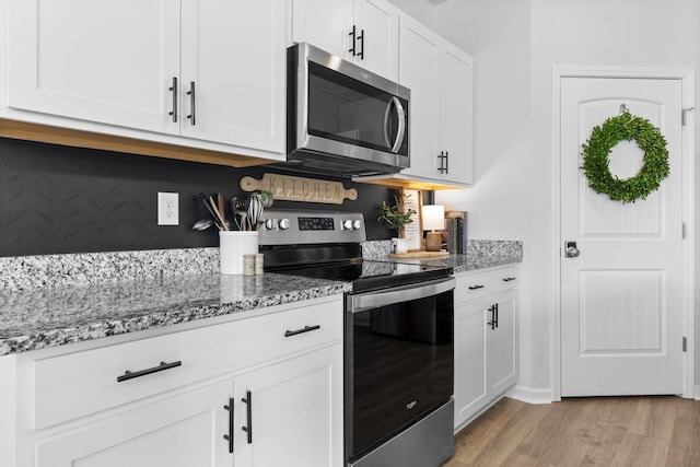 kitchen with stainless steel appliances, stone countertops, white cabinets, and light hardwood / wood-style flooring