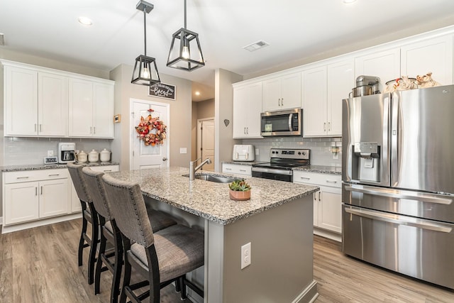 kitchen with sink, light stone counters, stainless steel appliances, a kitchen island with sink, and white cabinets