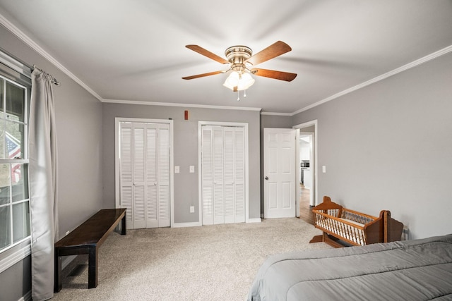 carpeted bedroom with ornamental molding, two closets, and ceiling fan