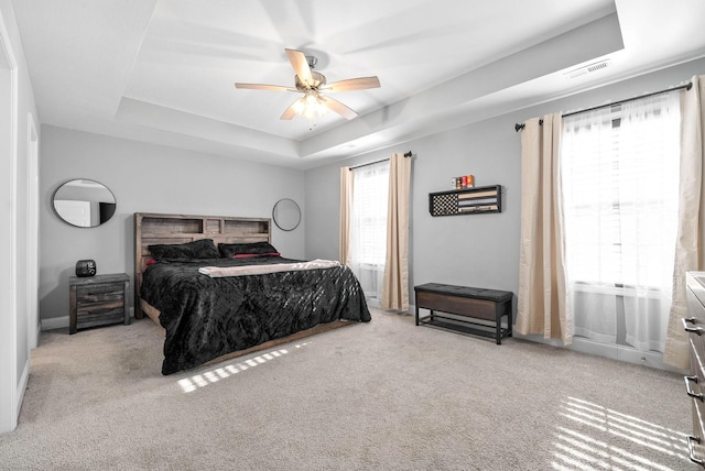 carpeted bedroom featuring a raised ceiling, ceiling fan, and multiple windows