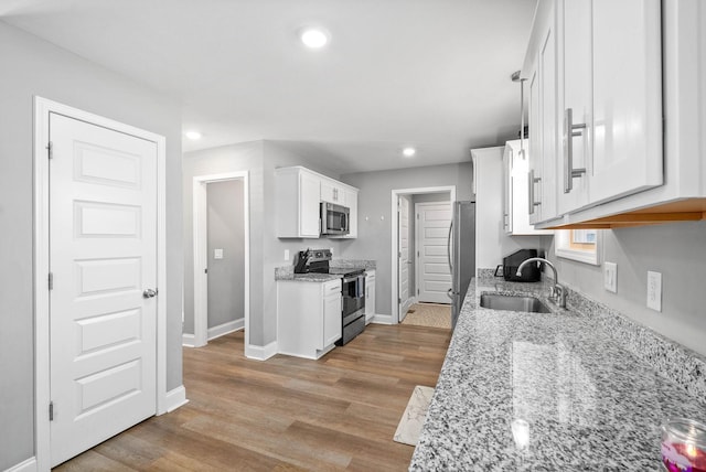 kitchen featuring sink, white cabinetry, stainless steel appliances, light stone counters, and decorative light fixtures