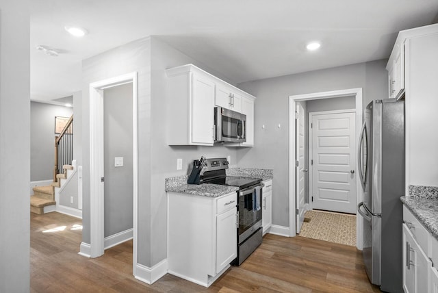 kitchen with dark wood-type flooring, stainless steel appliances, light stone countertops, and white cabinets