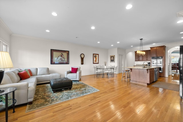 living room with sink, ornamental molding, light hardwood / wood-style floors, and a chandelier