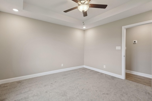 empty room featuring a raised ceiling, carpet flooring, and ceiling fan