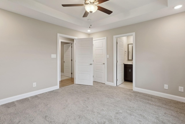 unfurnished bedroom featuring ensuite bath, light carpet, a raised ceiling, a closet, and ceiling fan