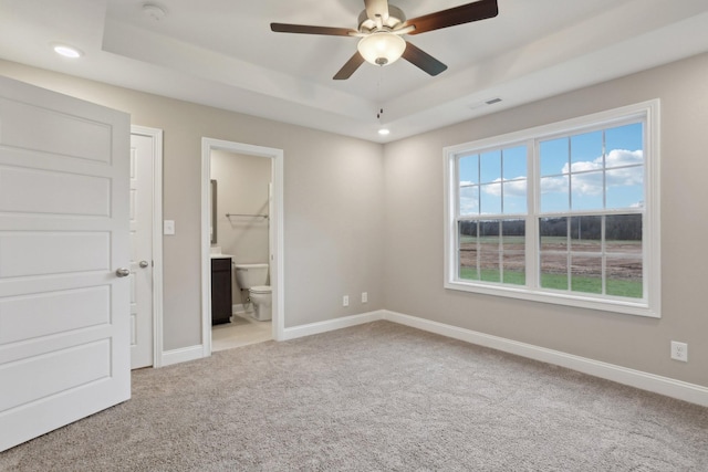 unfurnished bedroom featuring ceiling fan, connected bathroom, a tray ceiling, and light carpet