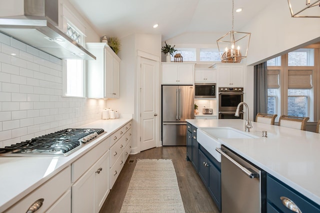 kitchen featuring blue cabinetry, white cabinetry, appliances with stainless steel finishes, pendant lighting, and range hood