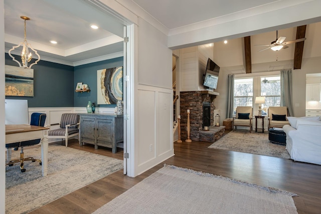 home office featuring ceiling fan with notable chandelier, hardwood / wood-style floors, ornamental molding, a stone fireplace, and beamed ceiling