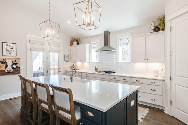 kitchen featuring pendant lighting, sink, white cabinets, a kitchen island with sink, and wall chimney exhaust hood