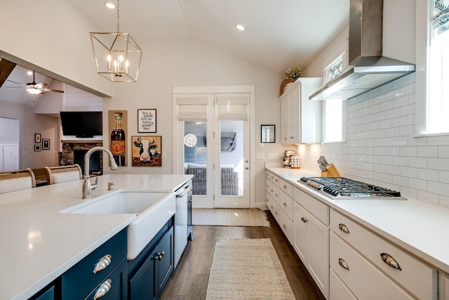 kitchen featuring wall chimney exhaust hood, blue cabinets, sink, decorative light fixtures, and stainless steel appliances