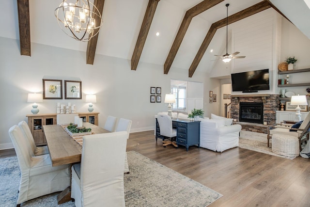 dining area featuring a stone fireplace, hardwood / wood-style floors, high vaulted ceiling, ceiling fan, and beam ceiling