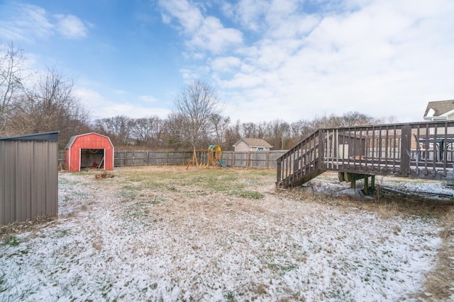 yard covered in snow featuring a storage shed, a playground, and a deck