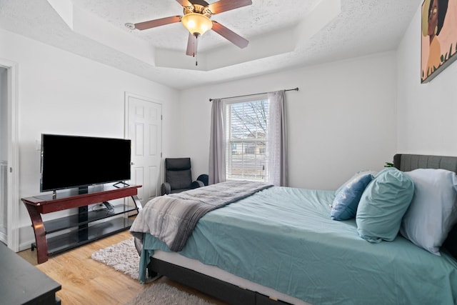 bedroom featuring ceiling fan, a tray ceiling, wood-type flooring, and a textured ceiling