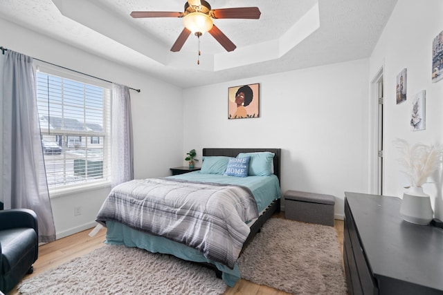 bedroom with light wood-type flooring, a textured ceiling, ceiling fan, and a tray ceiling