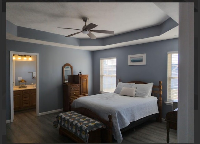 bedroom featuring ceiling fan, ensuite bathroom, dark hardwood / wood-style floors, and a raised ceiling