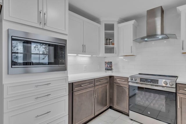 kitchen featuring built in microwave, white cabinets, decorative backsplash, stainless steel range with electric stovetop, and wall chimney exhaust hood