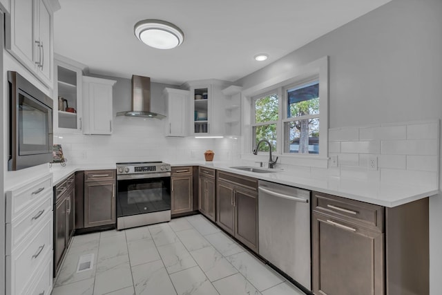 kitchen featuring wall chimney range hood, sink, appliances with stainless steel finishes, white cabinetry, and decorative backsplash