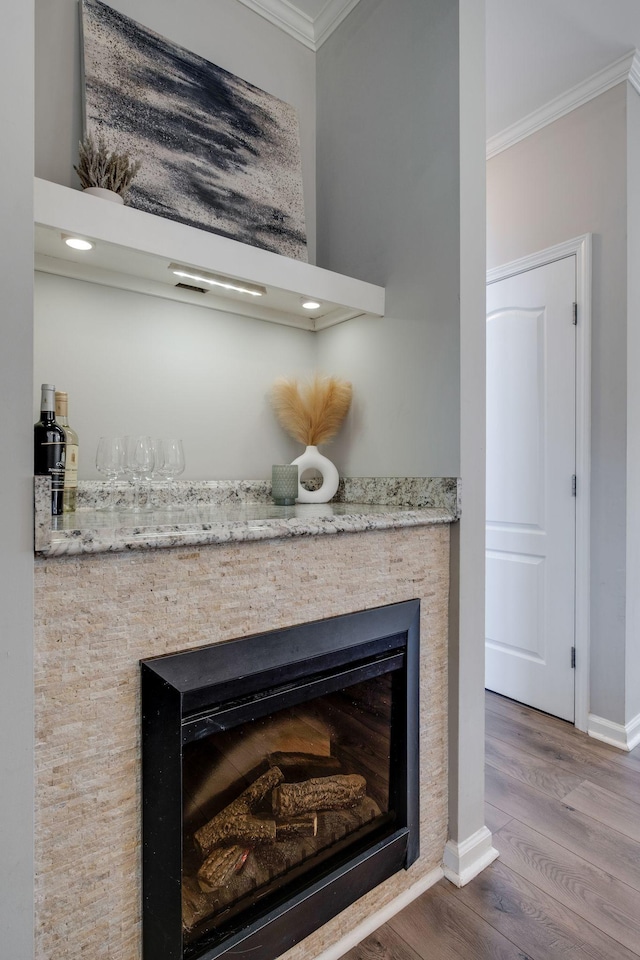 room details with crown molding, a stone fireplace, and hardwood / wood-style floors