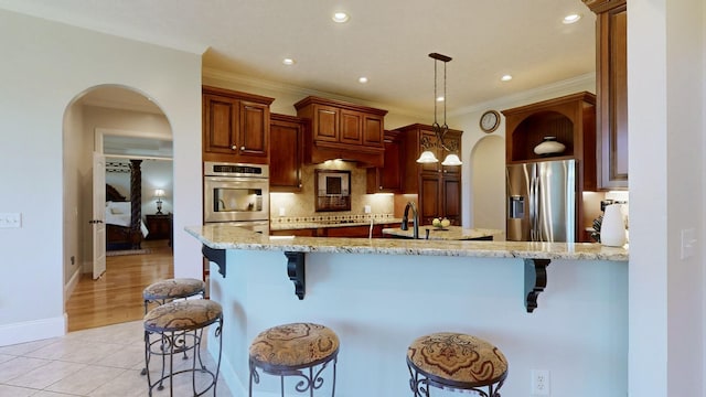 kitchen featuring pendant lighting, a kitchen breakfast bar, decorative backsplash, light tile patterned floors, and stainless steel appliances