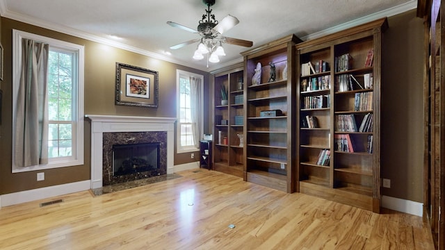 unfurnished room featuring a fireplace, ornamental molding, light hardwood / wood-style floors, and ceiling fan