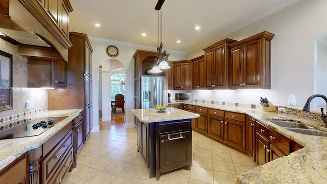 kitchen with light stone counters, sink, decorative light fixtures, and stainless steel fridge with ice dispenser