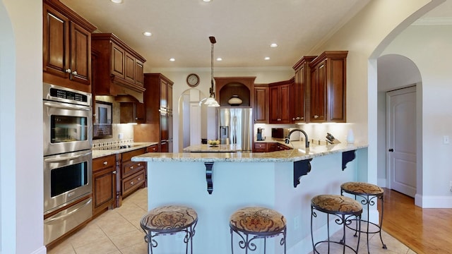 kitchen featuring light stone counters, crown molding, hanging light fixtures, a kitchen breakfast bar, and stainless steel appliances