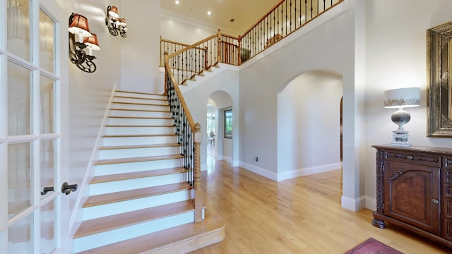 stairs with a high ceiling, wood-type flooring, and crown molding