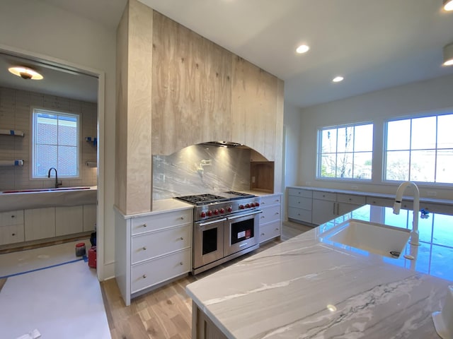 kitchen with tasteful backsplash, sink, double oven range, light stone counters, and light hardwood / wood-style floors