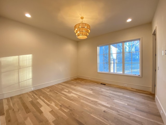 spare room featuring a chandelier and light hardwood / wood-style floors