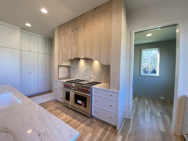 kitchen with sink, tasteful backsplash, light stone counters, light hardwood / wood-style flooring, and double oven range